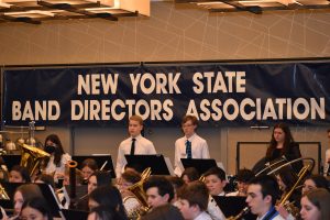 Three students standing in front of a banner that reads, "New York State Band Directors Association."