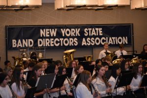 Students performing musical instrument. In the background there is a sign that reads, "New York State Band Directors Association."